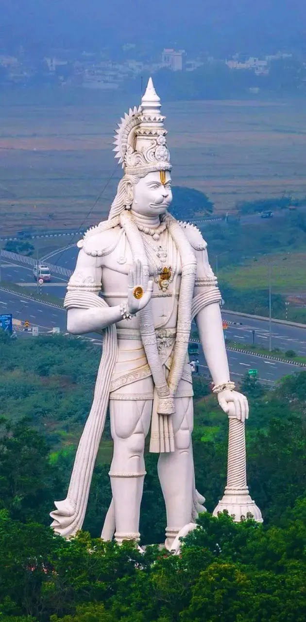 Giant Hanuman statue overlooks mountain landscape.