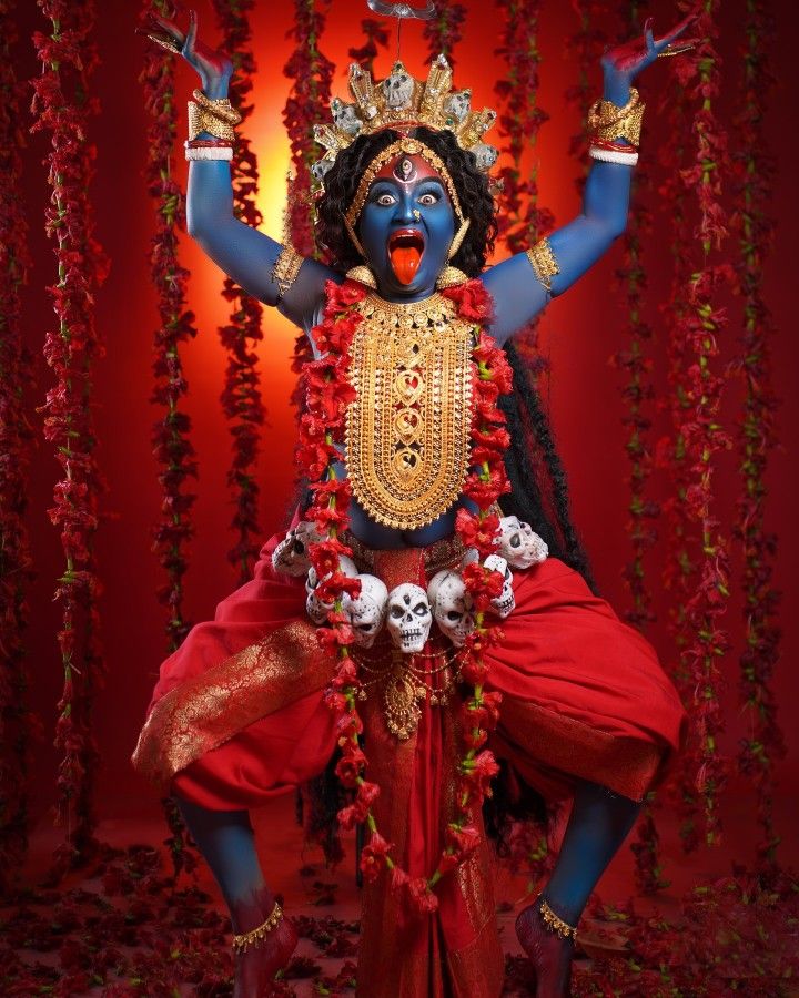 Maa Kali stands amidst crimson flowers.