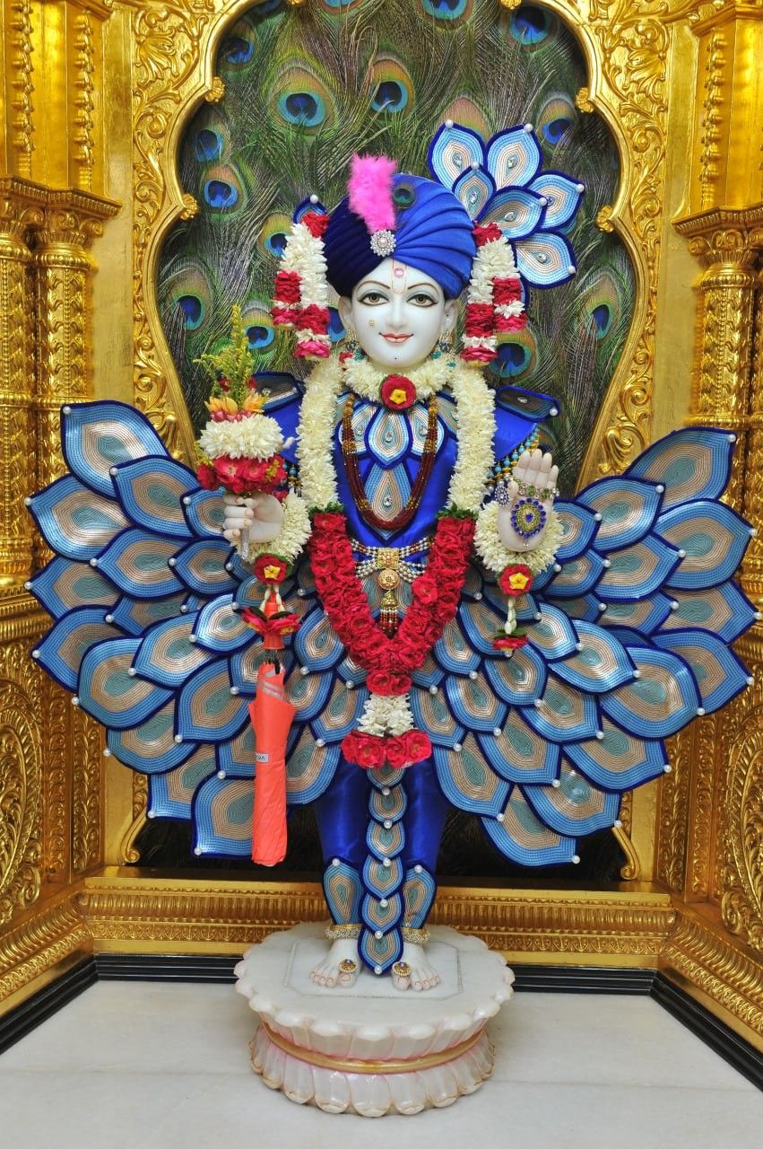 Swaminarayan with peacock feather backdrop.
